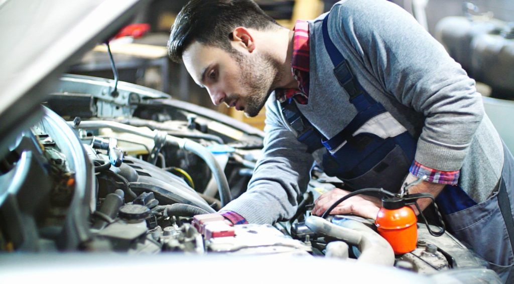 Car service technician looking under the hood of a car