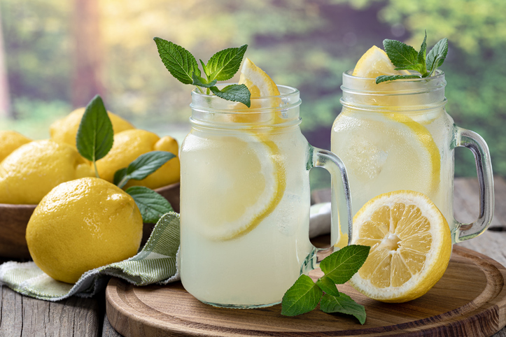 Two glasses of lemonade with mint and lemon on a wooden tray with rural background